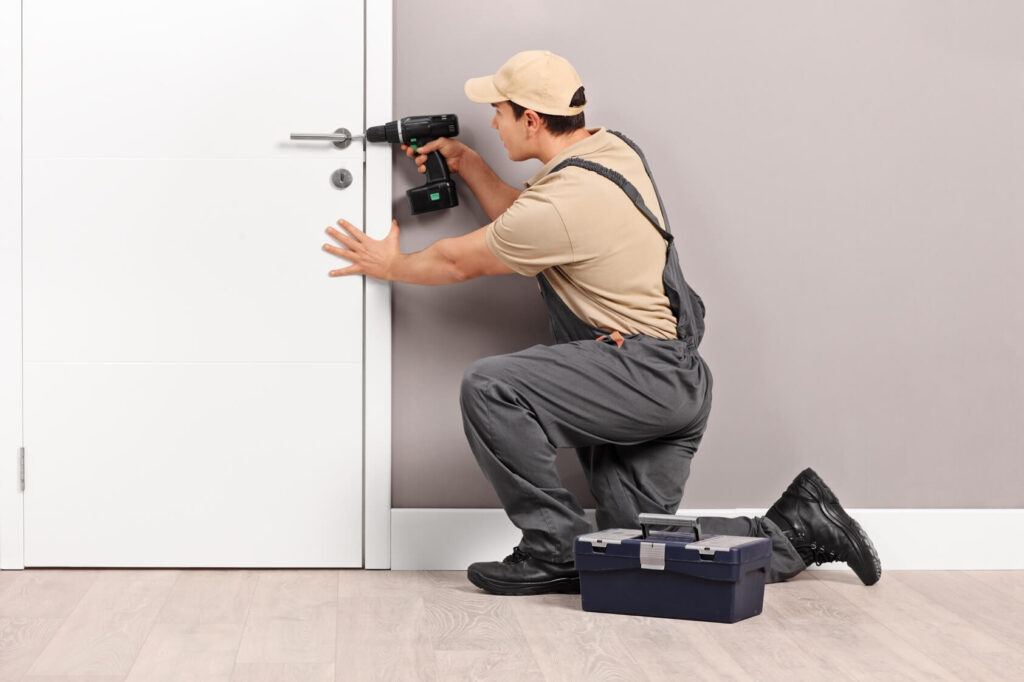 A locksmith uses a power drill to work on a door lock.