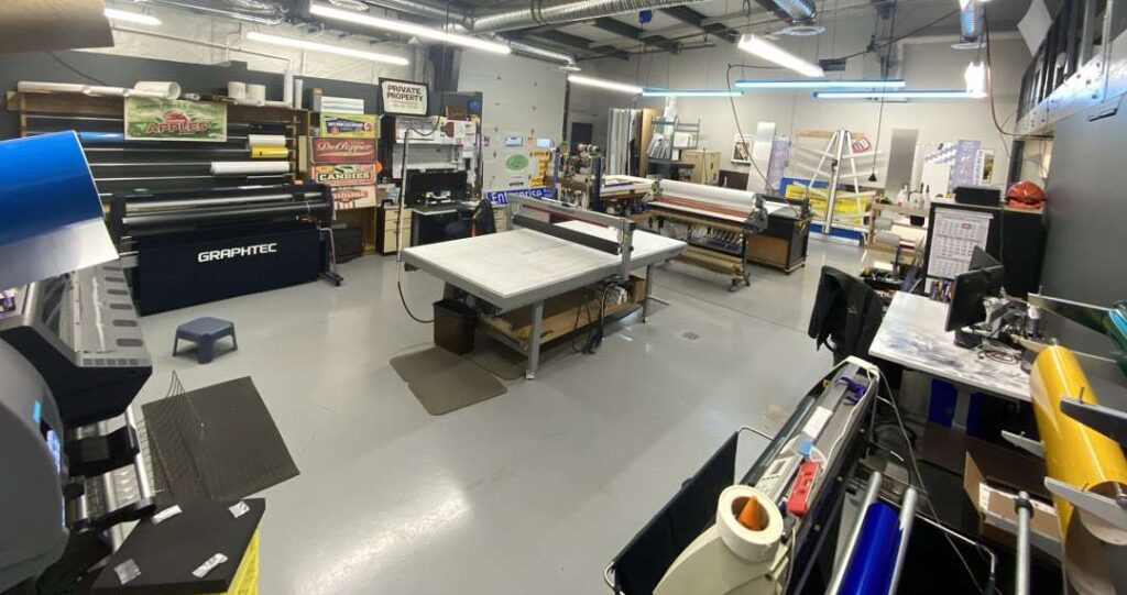 Printing workshop with wide-format printers and supply shelves.
