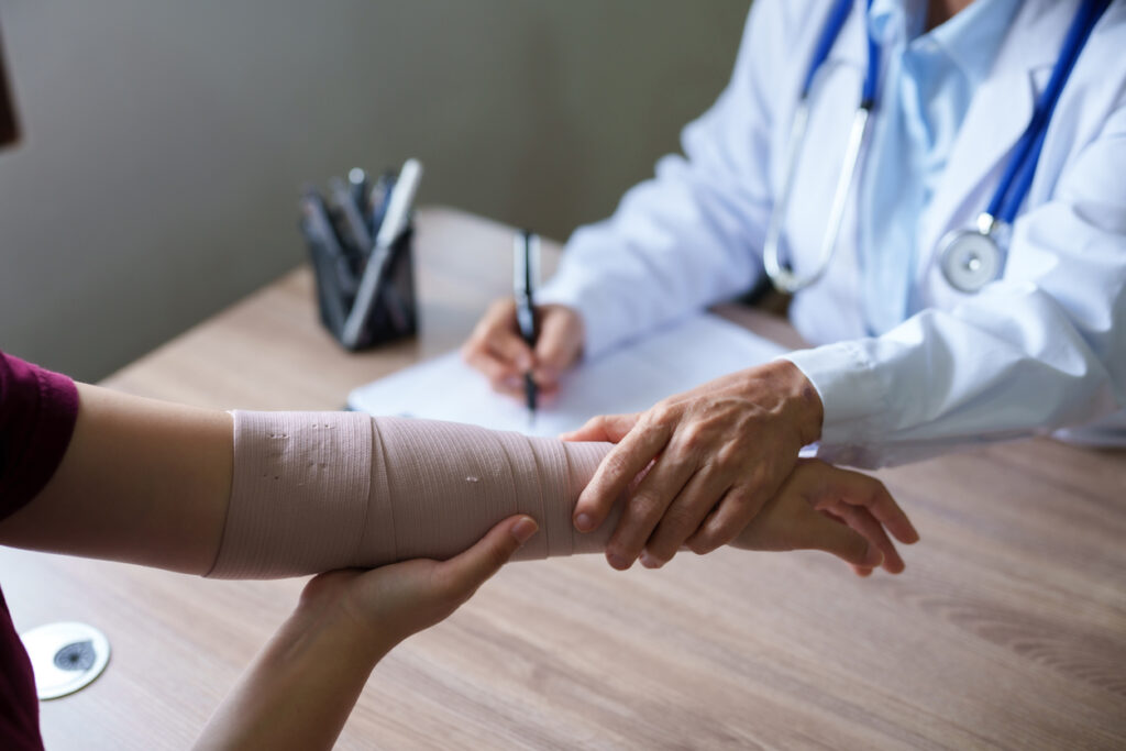 Doctor examines a patient’s arm wrapped in a compression bandage.