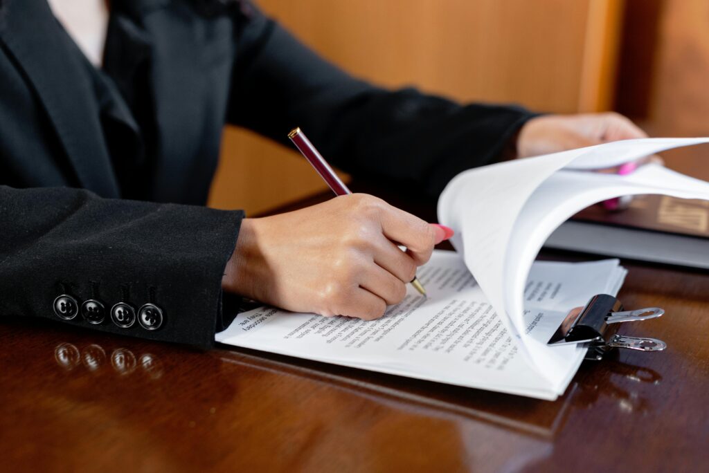 Person in a suit writing and reviewing documents at a desk.